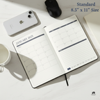 Open planner showing January 2025 on a white surface with a phone, mouse, and mug.