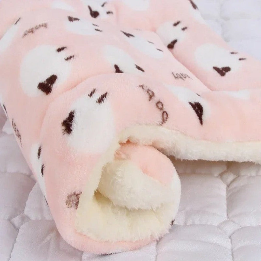 Pink plush blanket with brown heart patterns on a soft surface