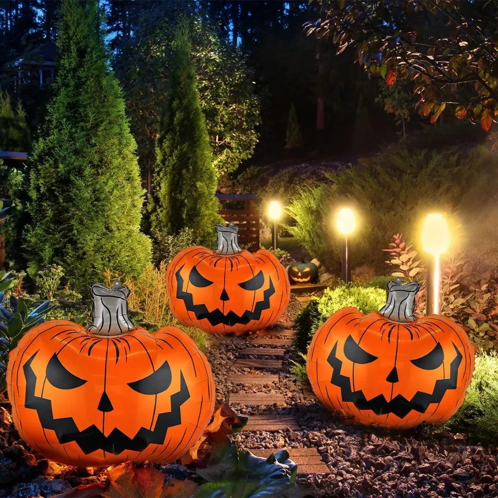 Three large inflatable jack-o'-lantern pumpkins with carved faces are arranged on a garden path at night, lit by warm pathway lights and surrounded by greenery.