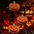 A collection of glowing jack-o'-lantern Halloween decorations displayed outdoors on a lawn at night, with some hanging from a tree and others clustered on the ground among fallen leaves.