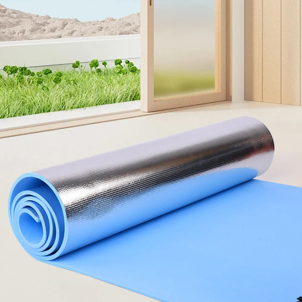 Roll of blue and silver insulation material on a floor with a window view of greenery outside.