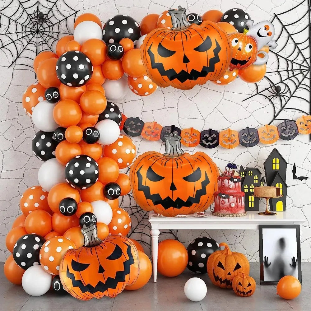 Halloween party decoration set featuring orange, black, and white balloons, inflatable jack-o'-lantern balloons, black spiderweb decals, a pumpkin banner, a small haunted house table decor, and a framed ghost photo frame on a light gray cracked-wall backdrop.